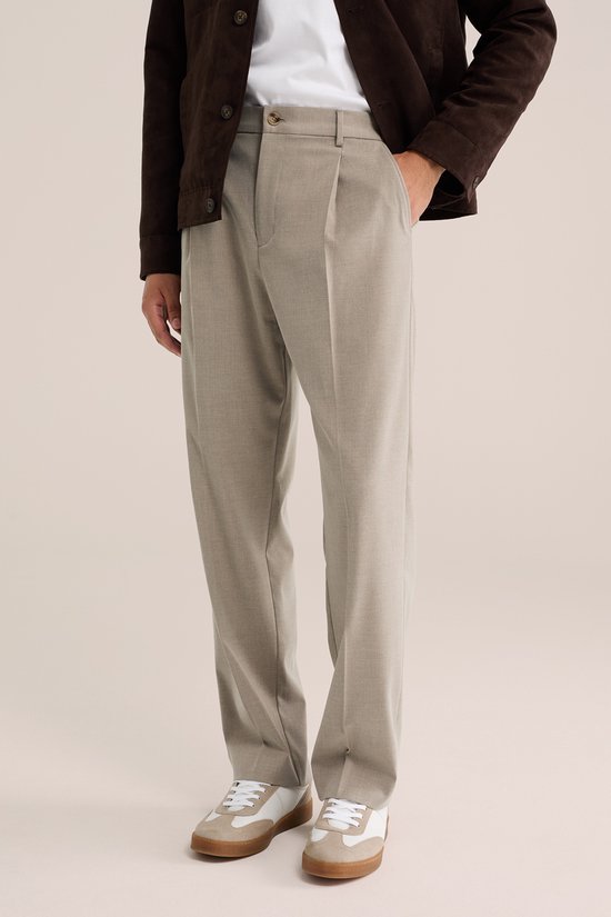 Man met donkerbruine jas, beige pantalon en witte sneakers.