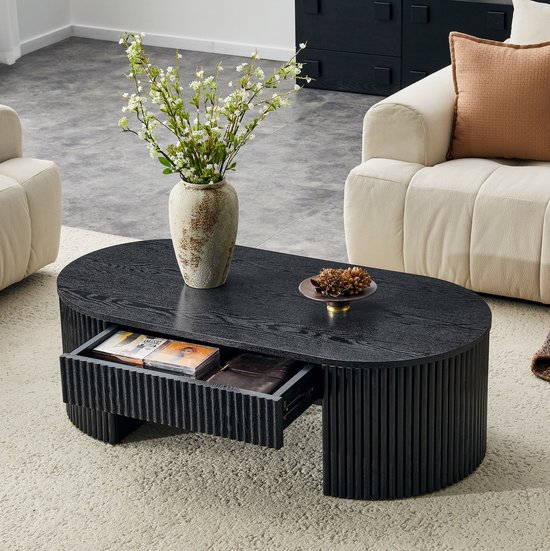Zwarte, ovale salontafel met verticale ribbels, een open lade met tijdschriften en een notitieboekje.