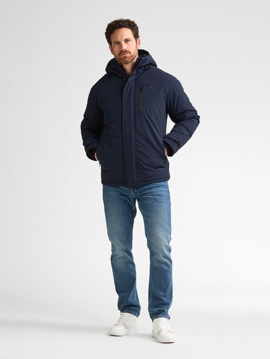 Man met donkerblauwe winterjas, spijkerbroek en witte sneakers.