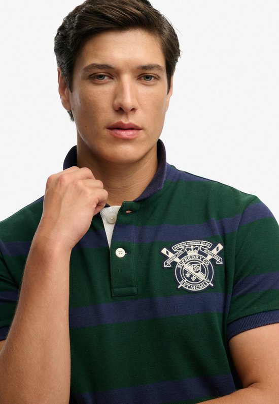 Donkergroen poloshirt met marineblauwe strepen en geborduurd logo op de borst.