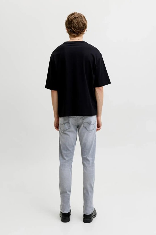 Achterkant van een man in een zwart t-shirt en grijze jeans met rechte pijpen.