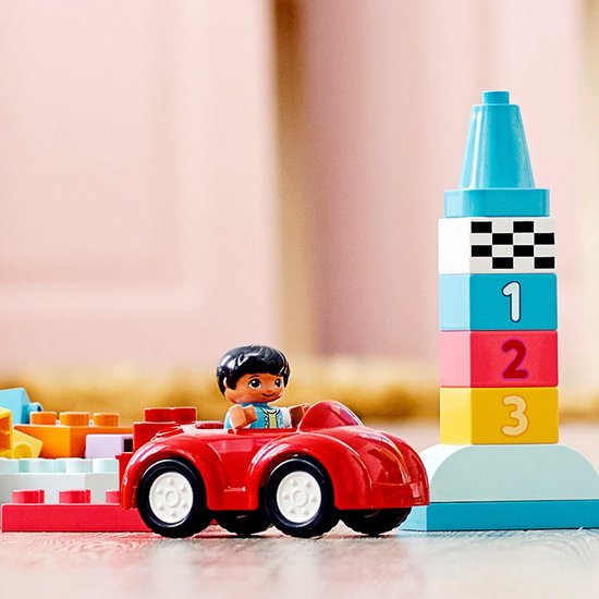 Voiture de course rouge avec un garçon, à côté d'une tour colorée avec des chiffres et un motif damier.
