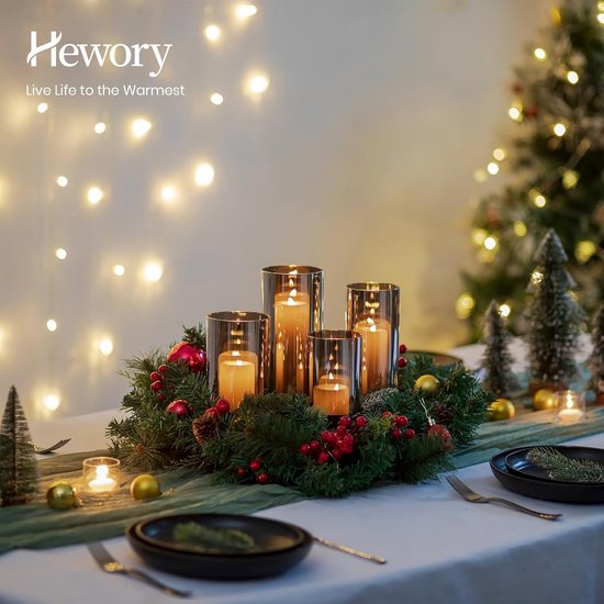 Een adventskrans met vier glazen windlichten met brandende kaarsen, versierd met dennentakken, rode bessen en dennenappels.