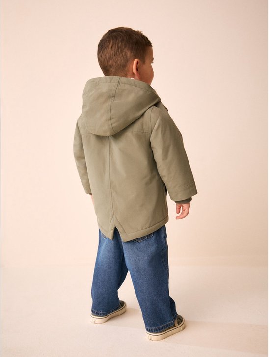 Achteraanzicht van een jongetje in een groene parka met capuchon, spijkerbroek en sneakers.