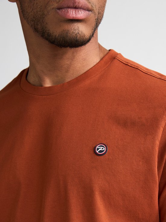 Close-up van een oranje t-shirt met een klein rond logo op de linkerborst.