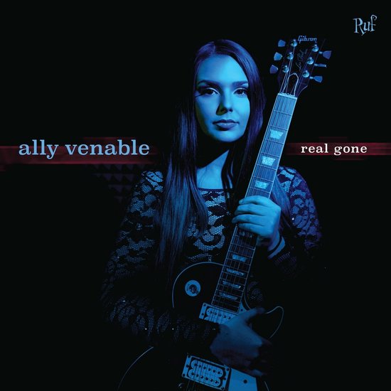Femme aux longs cheveux sombres, portant une robe noire en dentelle, tenant une guitare électrique.