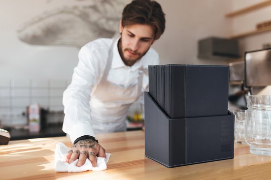 Zwarte menukaarten in een zwarte houder, terwijl een man een houten toonbank schoonmaakt.