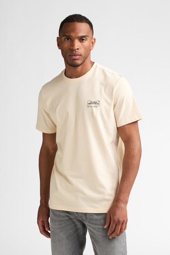 Man staat recht naar voren, draagt een crème T-shirt met opdruk en grijze jeans.