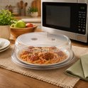 Transparant magnetrondeksel op een bord spaghetti met gehaktballen, naast een magnetron.