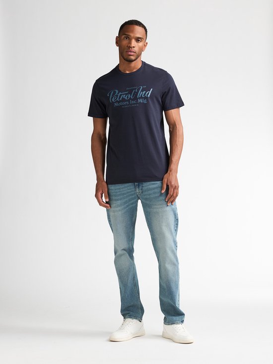 Model in marineblauw T-shirt met 'Petrol Ind Motors Inc. Mfg. Pennsylvania' print, gecombineerd met spijkerbroek.