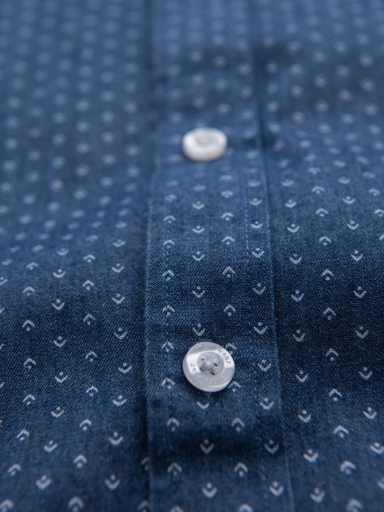 Close-up van de knopen van een blauw denim overhemd met witte stipjes.
