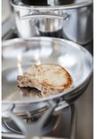 Bodem van een roestvrijstalen pan met een kort gebakken karbonade, op een gasfornuis.