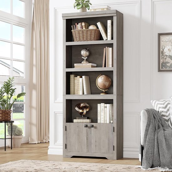 Grijze boekenkast opgesteld in een woonkamer, gevuld met boeken, decoratie en planten.