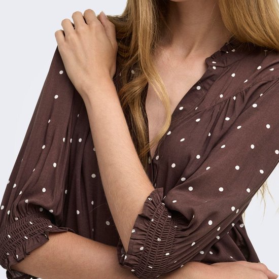 Detail van de bruine blouse met witte stippen en elastische manchetten aan de driekwart mouwen.