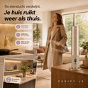Gouden FUSIFY LX diffuser op een houten tafel, met een vrouw die geniet van de geur in een interieur. "Je huis ruikt weer als thuis"