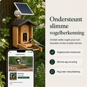 Vogelhuisje van bamboe met camera, een koolmees zit op de ladder. Telefoon toont vogelherkenning van koolmees.