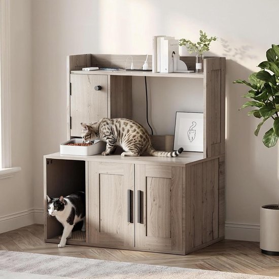 Grijs houten kattenmeubel met een kat die eet en een andere kat die uit de onderste kast komt. Boeken en planten op de bovenste plank.