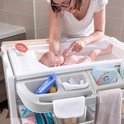 Baby in bad op de commode unit. Vrouw met bril verzorgt baby, met zeep en een olifantendoekje.