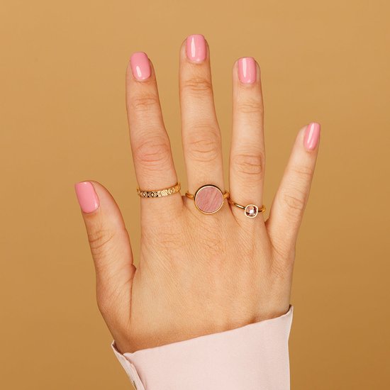 Hand met roze nagellak, met drie gouden ringen: een met een gestippeld patroon, een met een ronde steen en een met een kleine rode steen.