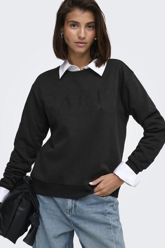 Model in zwarte sweater met parel "PARIS" opdruk, wit overhemd en jeans.