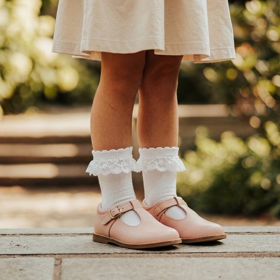 Meisjesbenen in witte sokken met kanten randje en roze T-bar schoenen.