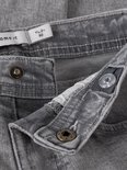 Detail van de tailleband van een grijze spijkerbroek met knopen en een label.