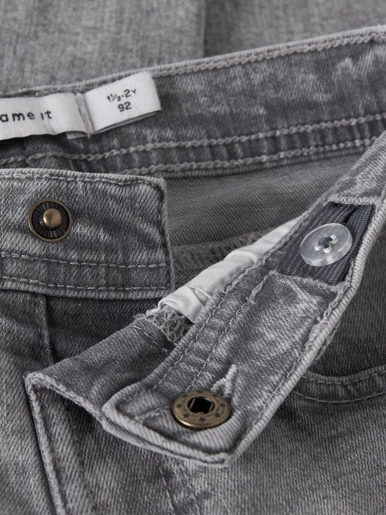 Detail van de tailleband van een grijze spijkerbroek met knopen en een label.