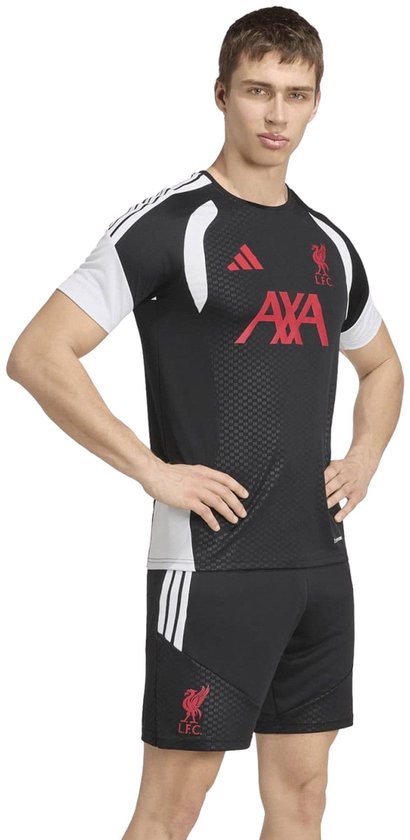 Man met zwarte Liverpool trainingstop met rode AXA-logo's en witte accenten. De hands-on-hips pose toont het sportieve design.