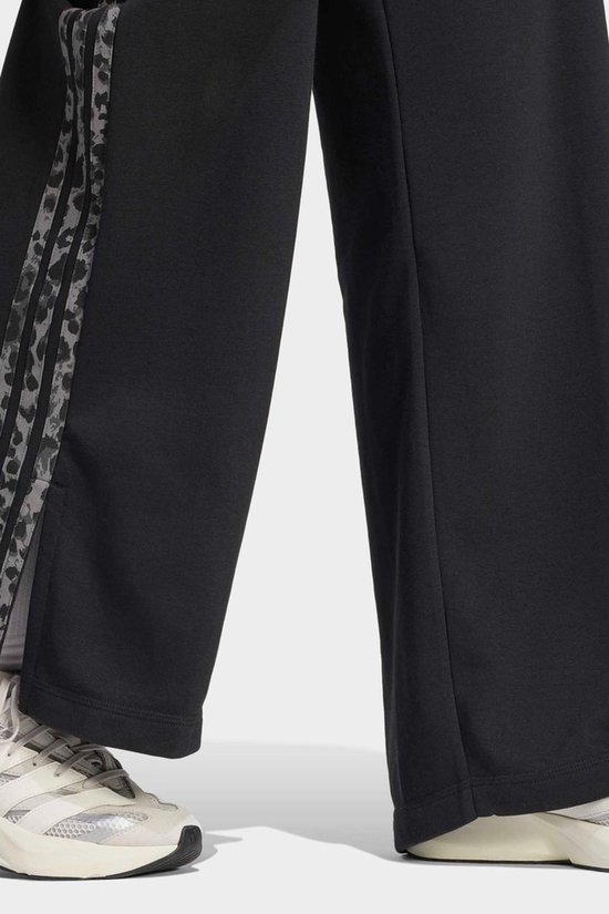 Detail van de zoom van een zwarte joggingbroek met een verticale streep in luipaardprint.