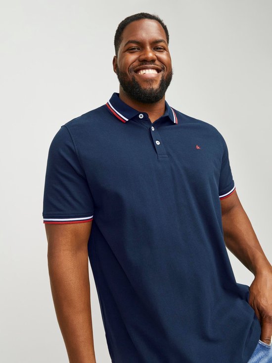 Donkerblauw poloshirt met witte en rode strepen op de kraag en mouwen, gedragen door een lachende man.