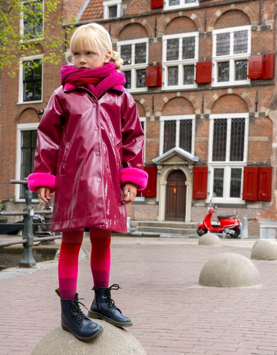 Kind draagt een bordeauxrode lakjas met felroze imitatiebont aan de kraag en mouwen, gecombineerd met een roze sjaal.