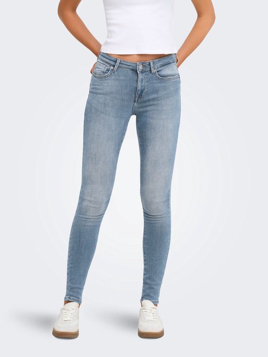 Model in een witte top en lichtblauwe skinny jeans, staand met handen in de zij.