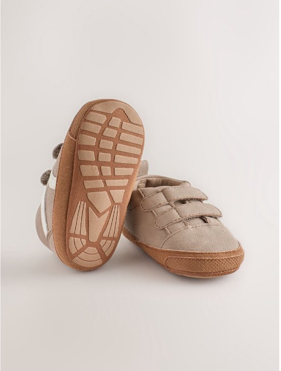 Zool en zijkant van bruine suède babysneakers met witte strepen en klittenbandsluiting.