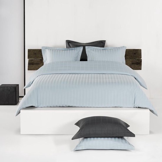 Lit fait avec une housse de couette bleu clair à rayures verticales et motif à carreaux.