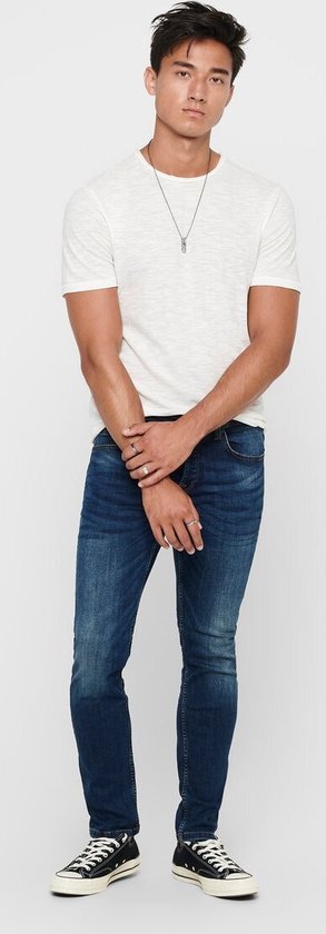 Man met wit gestreept T-shirt en donkerblauwe skinny jeans. Draagt zwarte sneakers.