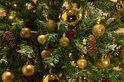 Kerstboom versierd met gouden kerstballen, dennenappels en lichtjes.