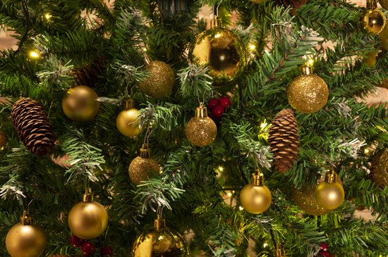Kerstboom versierd met gouden kerstballen, dennenappels en lichtjes.