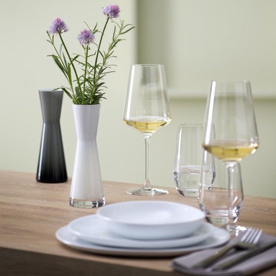 Un verre de vin blanc à côté d'un verre d'eau, sur une table avec des vases et des fleurs.
