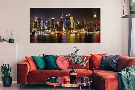 Un salon avec un canapé d'angle orange et une toile panoramique de la skyline nocturne de New York au mur.