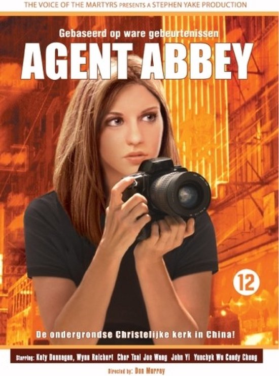 Een jonge vrouw met bruin haar, gekleed in een zwarte top, houdt een camera vast voor haar gezicht. De titel 'AGENT ABBEY' staat in grote witte letters boven haar.