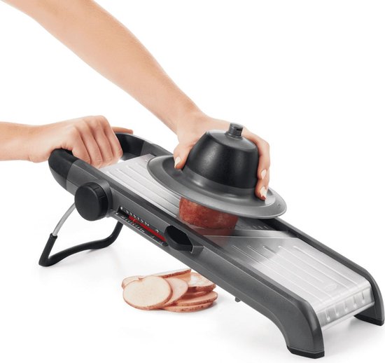 Handen gebruiken een mandoline om een aardappel te snijden, met gesneden aardappelschijfjes ernaast.