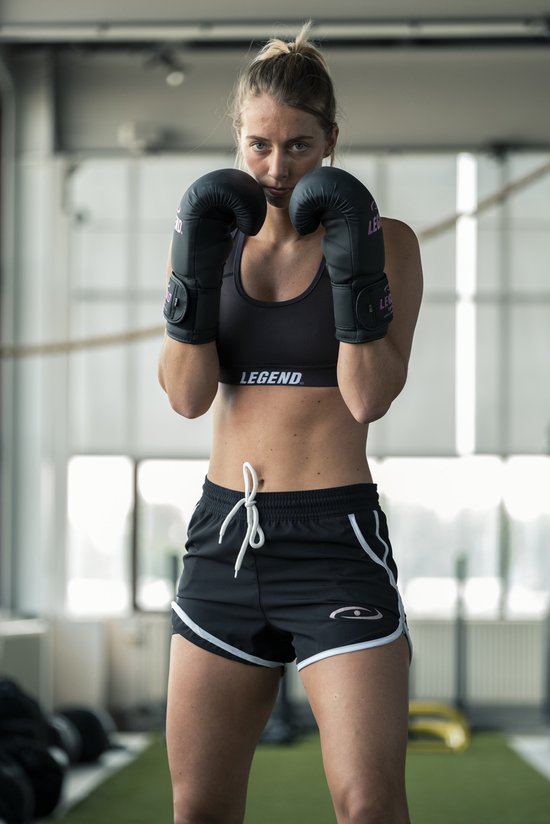 Vrouw met bokshandschoenen en sportbeha, in sportieve pose.