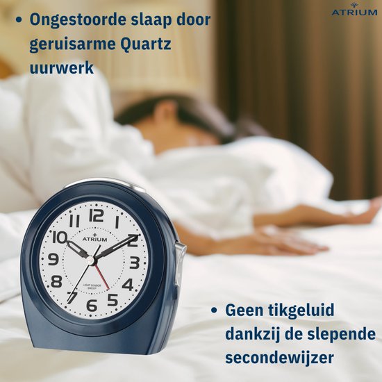Donkerblauwe wekker op een bed. Persoon slaapt op de achtergrond. Stil uurwerk.