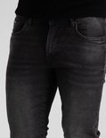 Close-up van de voorkant van een donkergrijze slim fit jeans met lichte scheuren.