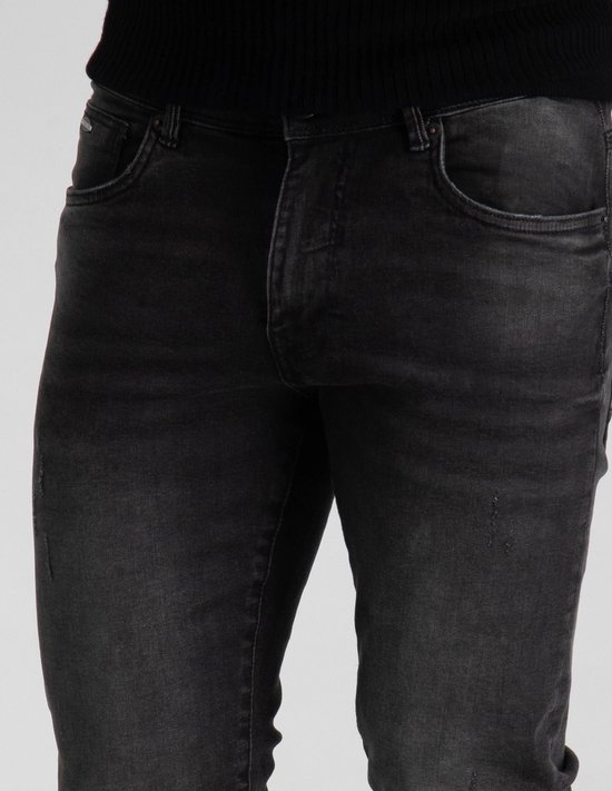 Close-up van de voorkant van een donkergrijze slim fit jeans met lichte scheuren.