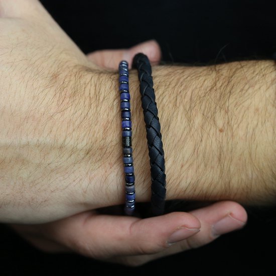 Twee herenarmbanden om een pols: een met blauwe kralen en zilveren accenten, de ander een zwarte gevlochten leren band.