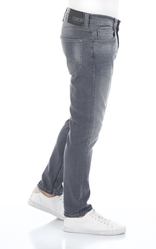 Man van de zijkant in een grijze Oregon tapered fit jeans van Mustang met witte sneakers.