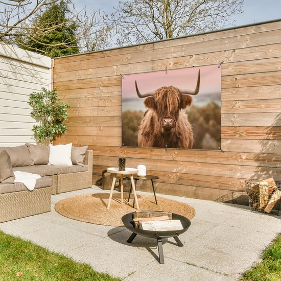 Un Highland coiffé de longues cornes, accroché à une clôture en bois dans un jardin avec un coin salon.