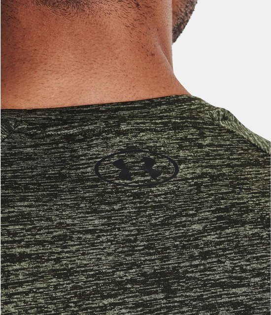 Close-up van het Under Armour logo op de nek van een olijfgroen gemêleerd sportshirt.