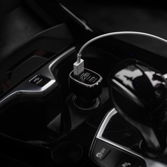 Zwarte REvall autolader met 3 USB-poorten, aangesloten op een witte kabel, in een auto-interieur.